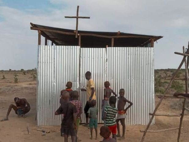 A tin chapel with a wooden cross, children gathered outside